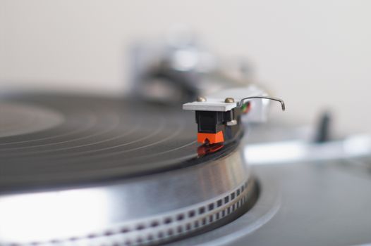 Turntable tone-arm cartridge playing vinyl record. Shallow depth of field
