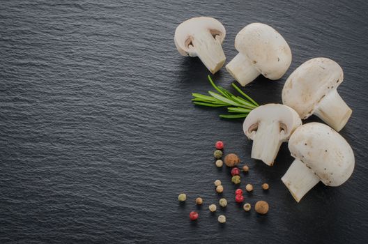 Fresh mushrooms with spices and herbs on a black board.
