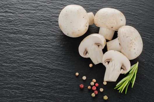 Fresh mushrooms with spices and herbs on a black board.