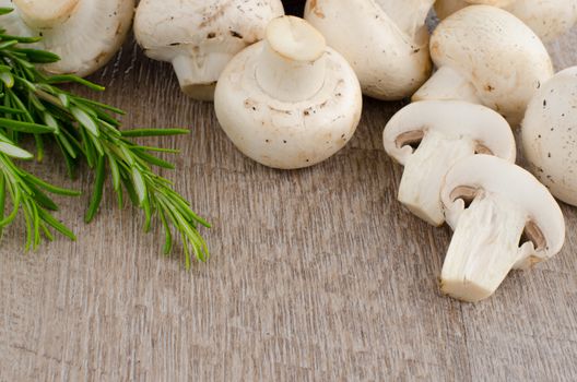 Fresh mushrooms with rosemary on a wooden background.