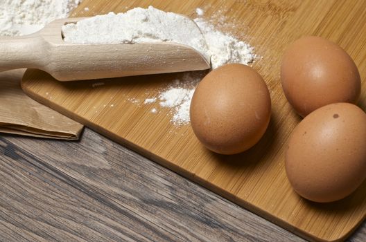 Eggs and flour with a wooden spoon on wooden background. 