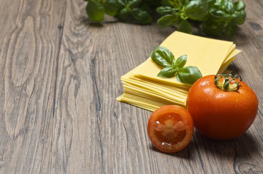 Raw pasta lasagna with basil leaves and fresh tomatoes on wooden background