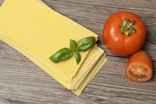 Raw pasta lasagna with basil leaves and fresh tomatoes on wooden background