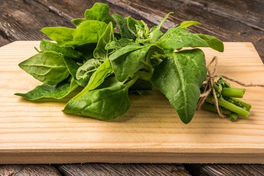 Spring spinach leaves on cutting board and dark wooden background