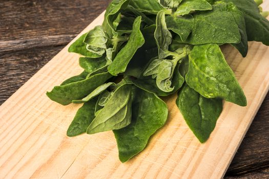 Spring spinach leaves on cutting board and dark wooden background