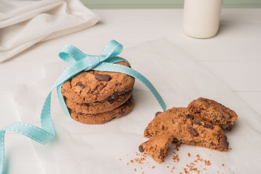 Chocolate chip cookies with a blue ribbon and a glass of milk on a white wooden table with a robin egg blue background. Vintage look.