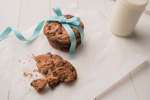 Chocolate chip cookies with a blue ribbon and a glass of milk on a white wooden table background. Vintage look.