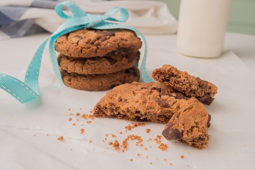 Chocolate chip cookies with a blue ribbon and a glass of milk on a white wooden table with a robin egg blue background. Vintage look.