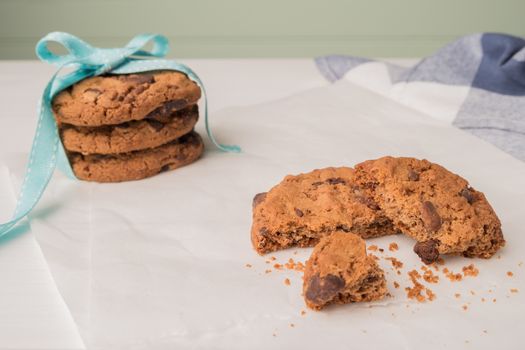 Chocolate chip cookies with a blue ribbon and a glass of milk on a white wooden table with a robin egg blue background. Vintage look.