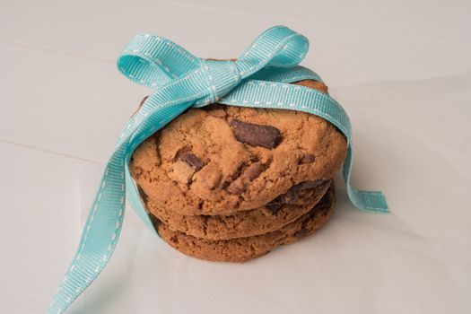 Chocolate chip cookies with a blue ribbon on a white wooden table background. Vintage look.