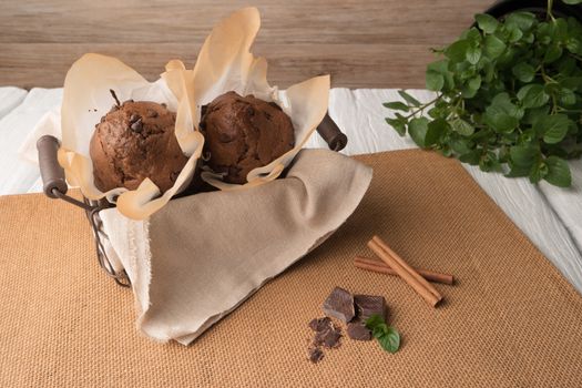 Chocolate muffins with chocolate slices in basket, cinnamom sticks and mint on placemat