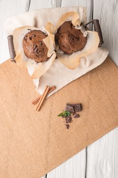 Chocolate muffins with chocolate slices in basket, cinnamom sticks and mint on placemat