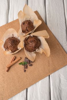 Chocolate muffins with chocolate slices in basket, cinnamom sticks and mint on placemat