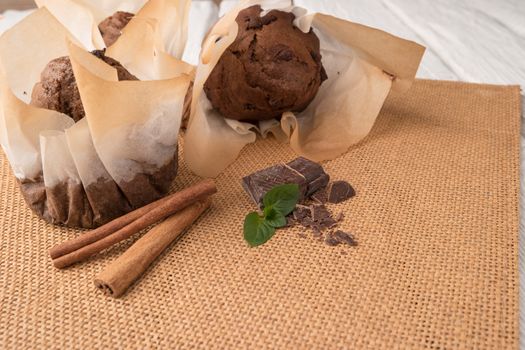 Chocolate muffins with chocolate slices in basket, cinnamom sticks and mint on placemat