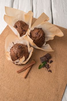 Chocolate muffins with chocolate slices in basket, cinnamom sticks and mint on placemat