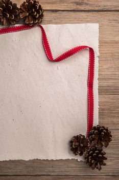 Christmas border design with pine cone and ribbon on parchment paper over old oak wood
