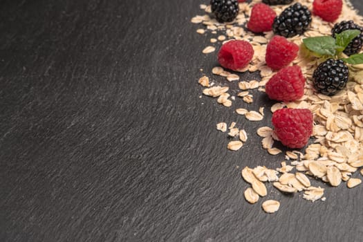 Healthy breakfast. Fresh granola, oatmeal with blackberries and raspberries on a black slate background. copy space