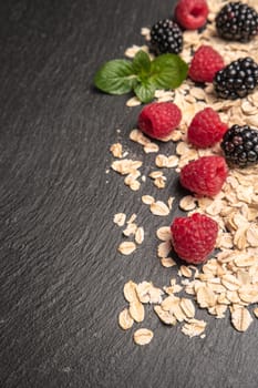 Healthy breakfast. Fresh granola, oatmeal with blackberries and raspberries on a black slate background. copy space