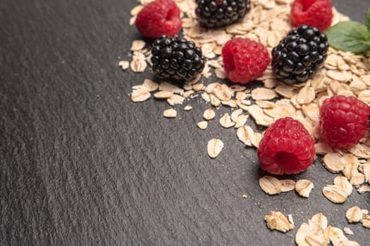 Healthy breakfast. Fresh granola, oatmeal with blackberries and raspberries on a black slate background. copy space