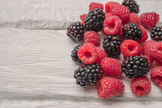 Ripe sweet raspberries and blackberries on wood table background