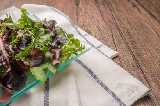 Fresh green salad with spinach, arugula, romaine and lettuce on plate. wood background