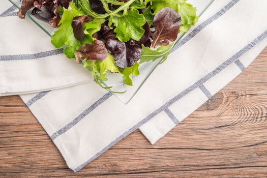 Fresh green salad with spinach, arugula, romaine and lettuce on plate. wood background