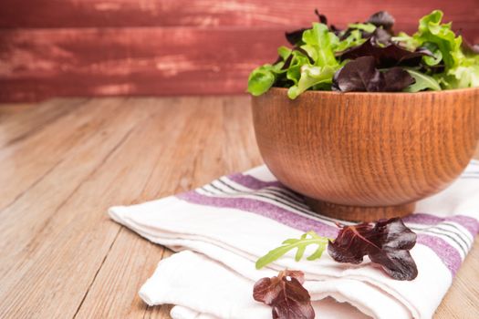 Fresh green salad with spinach, arugula, romaine and lettuce in a bowl on rustic wooden background