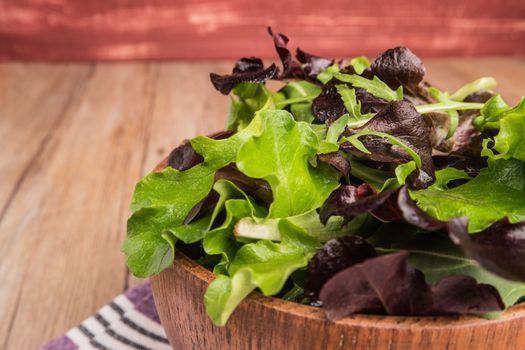 Fresh green salad with spinach, arugula, romaine and lettuce in a bowl on rustic wooden background