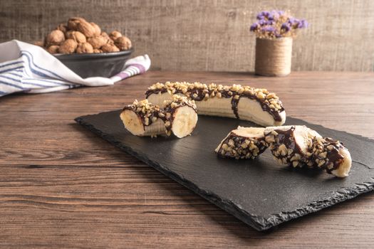 Fresh banana with melted chocolate and nuts coverage on slate