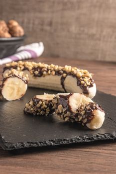 Fresh banana with melted chocolate and nuts coverage on slate