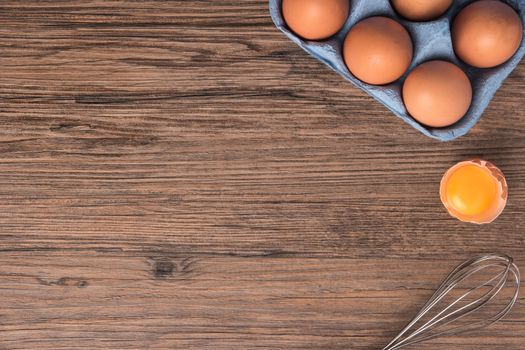 Cardboard egg box and egg beater on wooden table. Top view with copy space