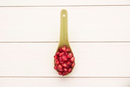 Seeds of red ripe peeled pomegranate on ceramic spoon. Rustic wood board background. Top view, copy space