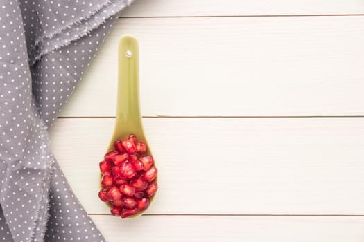 Seeds of red ripe peeled pomegranate on ceramic spoon. Rustic wood board background with polka dot fabric. Top view, copy space
