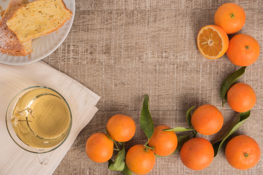 Slices of clementine cake with powdered sugar topping and cup of chamomile tea. Cake on a plate with fresh clementines on wooden board.