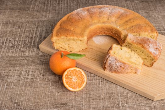 Slices of clementine cake with powdered sugar topping. Cake on a board with fresh clementines on wooden board.