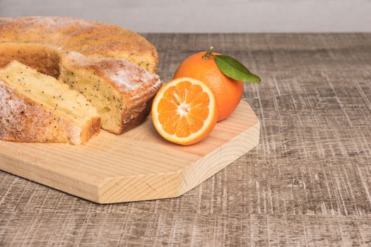 Slices of clementine cake with powdered sugar topping. Cake on a board with fresh clementines on wooden board.