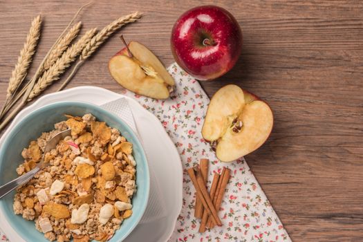 Healthy breakfast with muesli, red apple and cinnamon on rustic wooden table. Top view with copy space.