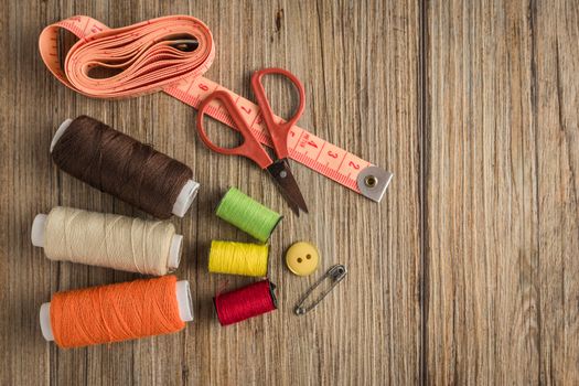 Sewing background. Accessories for needlework on wooden background. Spools of thread, scissors, buttons, measuring tape, sewing supplies. Set for needlework top view with copy space.