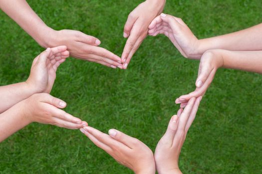 Many arms and hands of girls make heart shape above green grass