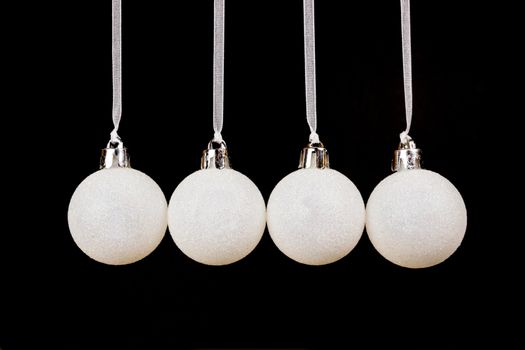 Four white christmas balls hanging in a horizontal row isolated on black background