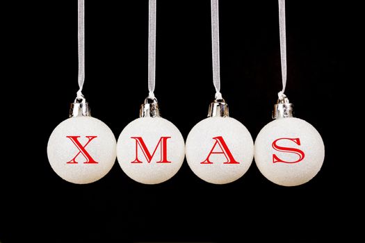 Word XMAS on white christmas balls hanging in a horizontal row isolated on black background