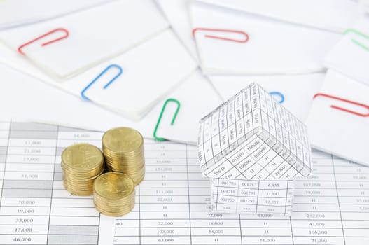 House and step pile of gold coins have step of paperwork with colorful paperclip on finance account.