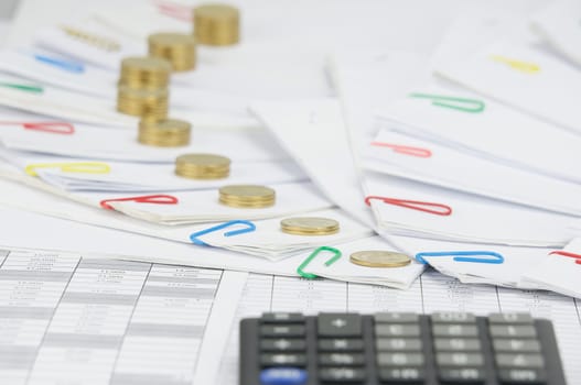 Step pile of gold coins on step of paperwork with colorful paperclip on finance account have blur calculator as foreground.