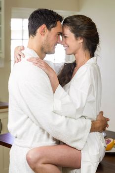 Romantic young couple in bathrobe cuddling each other in kitchen