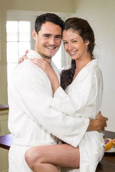Portrait of romantic young couple in bathrobe cuddling each other in kitchen