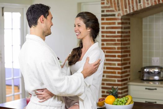 Romantic young couple in bathrobe cuddling each other in kitchen 