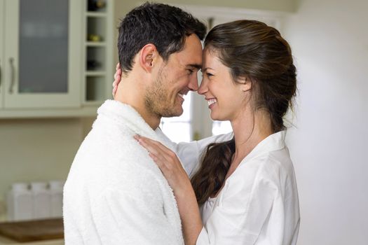Romantic young couple in bathrobe cuddling each other in kitchen