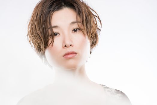 A high key headshot of a young and beautiful Japanese woman with a blurred lace sheet fluttering in front and cutting through the picture for artistic effect shot on a white background.