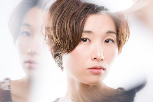 A high key headshot of a young and beautiful Japanese woman shot through mirrors arranged to get reflections around her face for artistic effect shot on a white background.