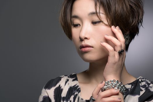 A portrait of a young, beautiful and very fashionable Japanese woman posed gently on a dark background.